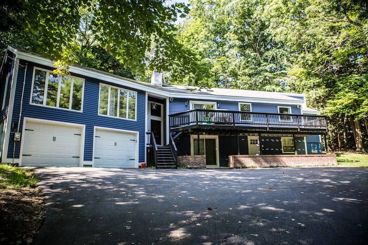 Blue vacation home with a deck, driveway, and leafy surroundings